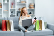 Young Woman Enjoying Online Shopping And Payment Using Credit Card At Home, Comfort and Technology Concept In a Cozy Living Space With Shopping Bags Around.