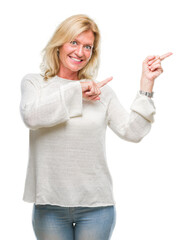 Sticker - Middle age blonde woman wearing winter sweater isolated background smiling and looking at the camera pointing with two hands and fingers to the side.