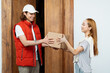 Friendly Delivery: Happy Courier In Red Vest Handing Over Package To Smiling Woman At Home. Service, Efficiency, Online Shopping.