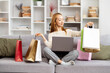 Young Woman Enjoying Online Shopping Success On Laptop, Surrounded By Colorful Shopping Bags In Cozy Home. Concept Of E-commerce, Happy, Satisfaction.