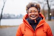 © CogniLens - Portrait of a happy afro-american woman in her 60s donning a durable down jacket over vibrant city park