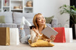 Online Shopping Bliss: Cheerful Young Woman With Digital Tablet And Credit Card, Surrounded By Shopping Bags, Enjoying a Relaxed Shopping Day at Home.