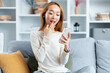 Surprised Young Woman Holding Smartphone At Home, Comfortable Home Setting With Modern Interior. Digital Lifestyle