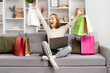 Joyful Young Woman Celebrates Online Shopping Success With Colorful Bags, Expressing Excitement And Happiness In Cozy Living Room.
