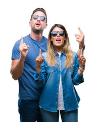 Poster - Young couple in love wearing sunglasses over isolated background amazed and surprised looking up and pointing with fingers and raised arms.