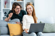 Happy Couple Shopping Online Together At Home. A Young Man Holding A Credit Card, Smiling Woman Browsing Laptop. Cozy, Connected, Leisure, E-Commerce Concepts