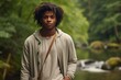 © CogniLens - Portrait of a satisfied afro-american man in his 20s wearing a chic cardigan in front of tranquil forest stream