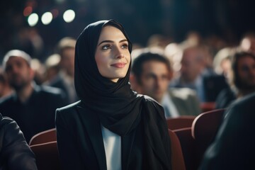 Wall Mural - A woman wearing a black scarf and a black jacket is sitting in a theater. She is smiling and looking at the camera