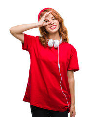 Canvas Print - Young beautiful hipster woman over isolated background wearing headphones and cap doing ok gesture with hand smiling, eye looking through fingers with happy face.