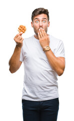 Poster - Young handsome man eating a sweet waffle over isolated background cover mouth with hand shocked with shame for mistake, expression of fear, scared in silence, secret concept