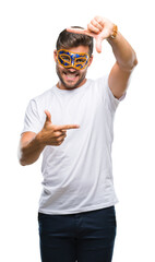 Sticker - Young handsome man wearing carnival mask over isolated background smiling making frame with hands and fingers with happy face. Creativity and photography concept.