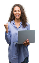 Wall Mural - Young hispanic woman holding computer laptop screaming proud and celebrating victory and success very excited, cheering emotion