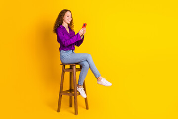 Wall Mural - Full body photo of pretty young girl sit chair hold device wear trendy violet outfit isolated on yellow color background