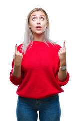 Poster - Young blonde woman wearing winter sweater over isolated background amazed and surprised looking up and pointing with fingers and raised arms.