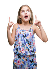 Wall Mural - Young beautiful girl wearing colorful dress over isolated background amazed and surprised looking up and pointing with fingers and raised arms.