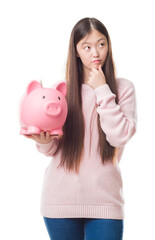 Wall Mural - Young Chinese woman over isolated background holding piggy bank serious face thinking about question, very confused idea