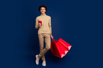 Sticker - Full size photo of nice young man hold device shopping bags wear trendy beige outfit isolated on dark blue color background