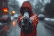 Figure in a crimson hoodie aims a gun at the camera in a snowy urban setting, evoking a tense and dramatic mood against a blurred city backdrop