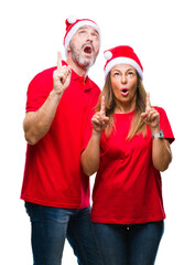 Wall Mural - Middle age hispanic couple wearing christmas hat over isolated background amazed and surprised looking up and pointing with fingers and raised arms.