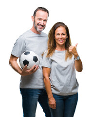 Canvas Print - Middle age hispanic couple holding football soccer ball over isolated background pointing and showing with thumb up to the side with happy face smiling