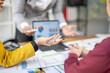 © Wasana - A woman is holding a pen and looking at a laptop. She is talking to another person who is looking at a piece of paper. The scene appears to be a meeting or a discussion about a project or a plan