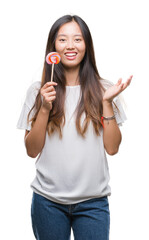 Sticker - Young asian woman eating lollipop candy over isolated background very happy and excited, winner expression celebrating victory screaming with big smile and raised hands