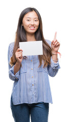 Sticker - Young asian woman holding blank card over isolated background surprised with an idea or question pointing finger with happy face, number one