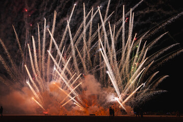 Vibrant fireworks illuminate the desert night sky in a captivating display of white, yellow, and red bursts. Spectacular scene at a music and art festival.