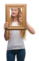 Sticker - Blonde teenager woman holding vintage frame art doing ok sign with fingers, excellent symbol