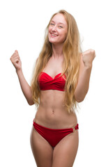 Poster - Blonde teenager woman wearing red bikini very happy and excited doing winner gesture with arms raised, smiling and screaming for success. Celebration concept.