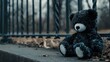 © AkuAku - On a dreary day at the playground a forlorn black and white teddy bear sits beside a metal fence its lonely and sorrowful expression mirroring its solitude Abandoned in the park this lost to