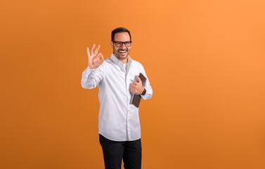 Portrait of happy businessman with laptop computer showing OK sign and posing on orange background