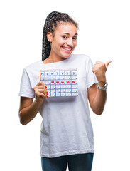 Poster - Young braided hair african american girl holding menstruation calendar over isolated background pointing and showing with thumb up to the side with happy face smiling