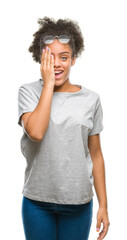 Wall Mural - Young afro american woman wearing glasses over isolated background covering one eye with hand with confident smile on face and surprise emotion.