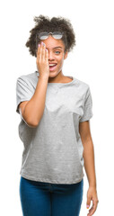 Canvas Print - Young afro american woman wearing glasses over isolated background covering one eye with hand with confident smile on face and surprise emotion.