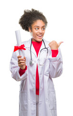 Wall Mural - Young afro american doctor woman holding degree over isolated background pointing and showing with thumb up to the side with happy face smiling
