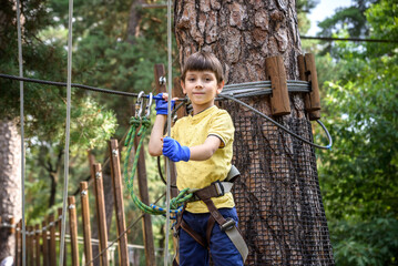 Wall Mural - Strong excited young boy playing outdoors in rope park. Caucasian child dressed in casual clothes and sneakers at warm sunny day. Active leisure time with children concept