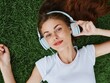 Beautiful woman in headphones listening to music lying on the grass on the lawn in the park in the spring and a smile with teeth, the concept of health and recreation in nature, mental health