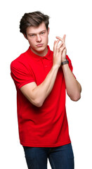 Wall Mural - Young handsome man wearing red t-shirt over isolated background Holding symbolic gun with hand gesture, playing killing shooting weapons, angry face