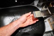 A man's hand touches the water and washes his hands with soap. A black sink with a silver faucet next to an oval mirror and a shelf with hand paper towels. Close-up 