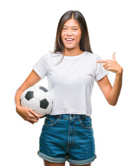 Canvas Print - Young asian woman holding football soccer ball over isolated background with surprise face pointing finger to himself