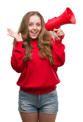 Canvas Print - Young blonde woman holding red megaphone very happy and excited, winner expression celebrating victory screaming with big smile and raised hands