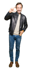 Wall Mural - Middle age handsome man wearing black leather jacket smiling and confident gesturing with hand doing size sign with fingers while looking and the camera. Measure concept.