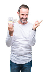 Sticker - Senior hoary man holding buch of dollars over isolated background very happy pointing with hand and finger to the side