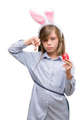 Poster - Young blonde child wearing easter bunny ears with angry face, negative sign showing dislike with thumbs down, rejection concept