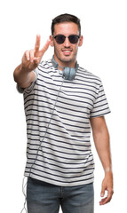 Wall Mural - Handsome young man wearing headphones smiling looking to the camera showing fingers doing victory sign. Number two.