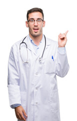 Canvas Print - Handsome young doctor man with a big smile on face, pointing with hand and finger to the side looking at the camera.