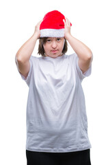 Wall Mural - Young adult woman with down syndrome wearing christmas hat over isolated background suffering from headache desperate and stressed because pain and migraine. Hands on head.