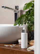 Lotion pump bottle near basin and green plant on wooden countertop in bath, cosmeticmockup