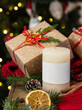 Pillar candle with label near wrapped Christmas gift, red sweater and decor, winter mockup